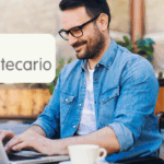 Hombre sonriente usando un laptop mientras trabaja en un café, con el logo de Banco Hipotecario visible en la esquina superior izquierda.