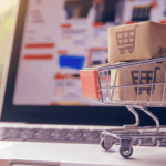 Carrito de compras con paquetes sobre una laptop, representando el e-commerce como opción para tener ingresos extra en Argentina.